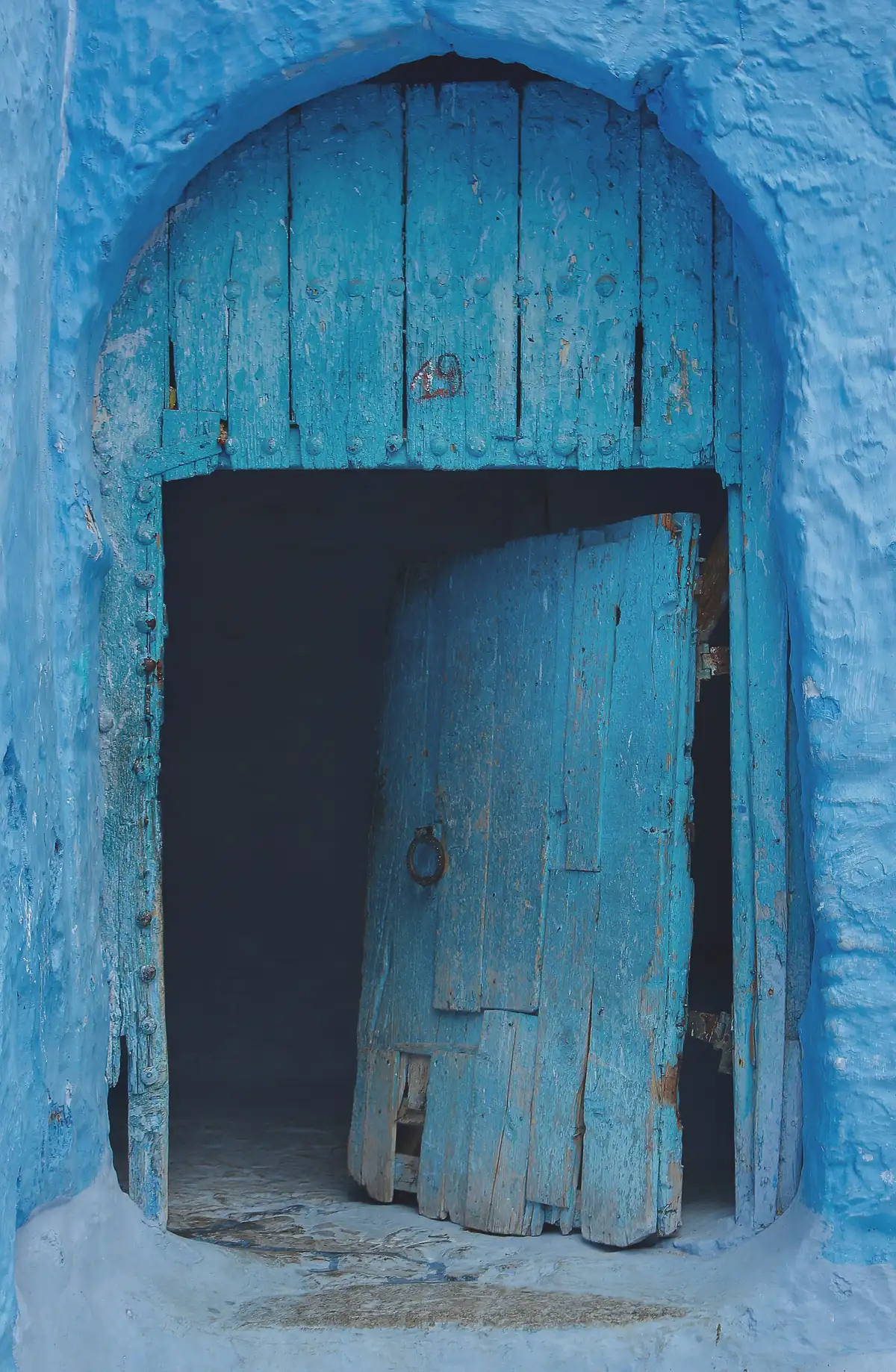 Weathered blue wooden door set into a blue-washed wall in the Chefchaouen medina