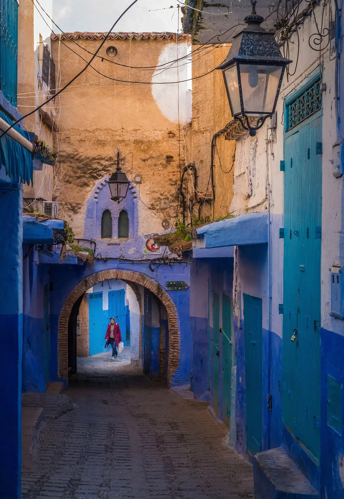 Woman walking through a stone archway between blue-washed houses in the Chefchaouen medina